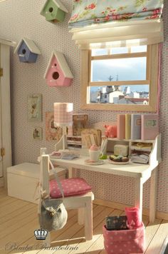 a dollhouse desk and chair in a room with pink curtains, bird houses, and other items on the table