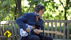 a man sitting on a bench playing an electric guitar and singing into a microphone while wearing headphones