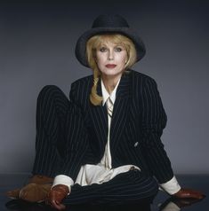 a woman sitting on the ground wearing a suit and hat