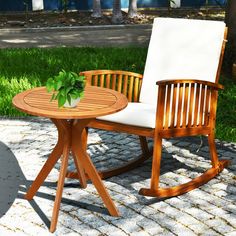 a wooden rocking chair and table with a plant on it in the middle of a yard