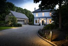 a large house that is lit up at night with lights on the driveway and trees around it