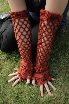 a woman is sitting on the grass with her hands in crocheted gloves