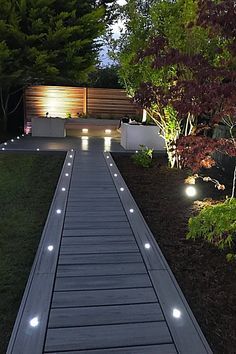 a walkway lit up at night with lights on it and some trees in the background