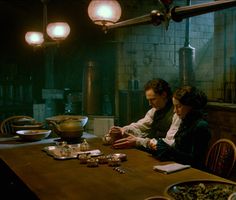 two people sitting at a table in a dark room with food on the table and lights hanging from the ceiling