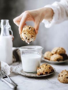 a person holding a cookie in their hand over a glass of milk and cookies on the table