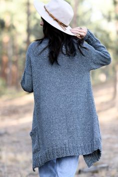 a woman with long hair wearing a hat and sweater in the woods, back view