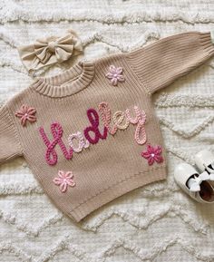 a knitted sweater with the word baby written on it next to shoes and sunglasses