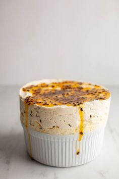 a cake in a white dish sitting on a marble counter top with orange sauce drizzled over it