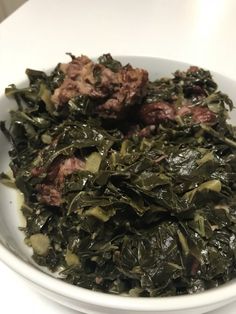 a white bowl filled with greens and meat