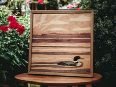 a wooden duck sitting on top of a table next to some red and pink flowers