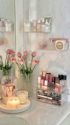 a bathroom counter with pink flowers and candles on it, along with other makeup products