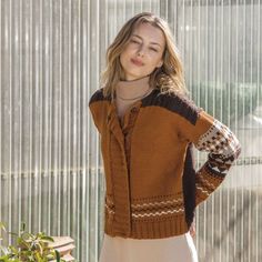 a woman standing in front of a window wearing a brown sweater and tan skirt with white stripes on the sleeves