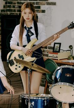 a girl with long hair is holding a guitar and standing in front of two drums