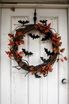 a wreath with bats hanging from it on the front door is decorated with orange and green leaves