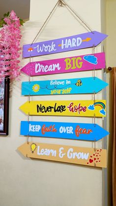 colorful wooden signs hanging from a wall next to a vase with pink flowers in it