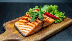 a piece of salmon on a wooden cutting board with lettuce and red peppers