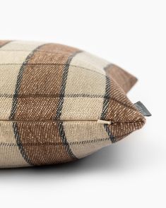 a brown and black plaid pillow on a white surface with a tag in the middle