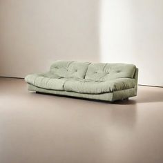 a green couch sitting on top of a floor next to a white wall in an empty room