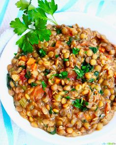 a white plate topped with lentils and garnished with cilantro leaves