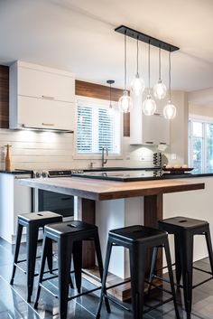 a kitchen island with stools and lights hanging from it