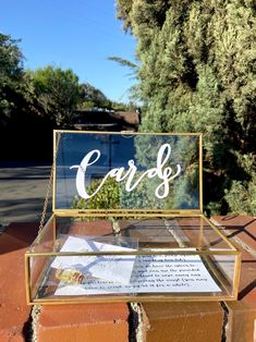 a clear glass box with the word cards on it sitting on top of a brick wall