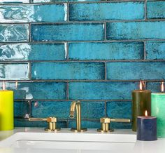 three candles sitting on top of a white sink next to a blue tiled backsplash