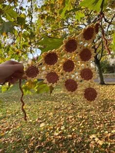 someone is holding up a crocheted doily in front of a tree with leaves on the ground