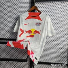 a white shirt with red and yellow designs is hanging on a metal rack in front of a fence