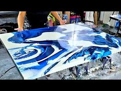 a table that has been painted with blue and white fluid paint on it, while someone is working in the background