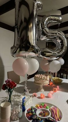 a table topped with balloons and cake next to a giant number balloon in the air