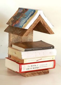 a stack of books sitting on top of a wooden house shaped like a birdhouse