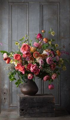 a vase filled with lots of colorful flowers on top of a wooden table next to a wall