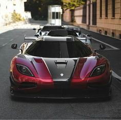 a row of red and black sports cars parked on the side of a road in front of a building