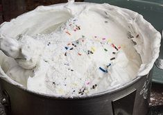 a bucket filled with white frosting and sprinkles on top of a table