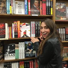 a woman standing in front of a bookshelf with many books on the shelves