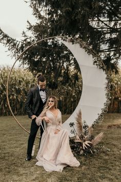 a man and woman standing next to each other in front of a large moon sculpture