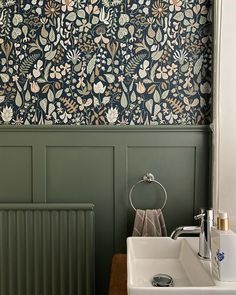 a bathroom with green walls and floral wallpaper in the corner, along with a white sink