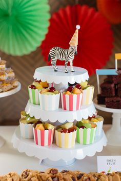 a zebra figurine stands on top of cupcakes that are stacked high