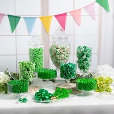 a table topped with lots of green candies and lollipops in glass containers