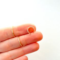 a woman's hand holding two rings in her left hand, one with an orange stone on it