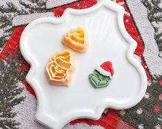 two cookies shaped like christmas trees on a white platter with red and green decorations