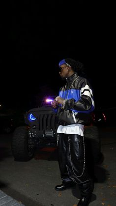 a man standing in front of a black jeep at night wearing a blue and white jacket