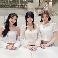 three young women sitting on top of a white bed