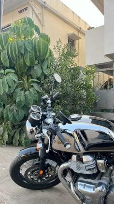 a black motorcycle parked next to a green bush and building on the side of the road