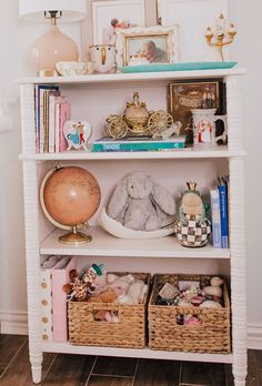 a white book shelf with baskets and stuffed animals on it's top, next to a lamp