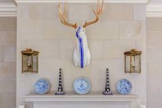 the fireplace is decorated with blue and white plates, deer head on the mantel