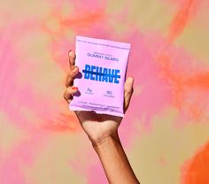 a person holding up a pink package with the words shine on it in front of a colorful background