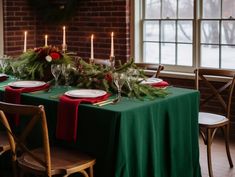 the table is set for christmas dinner with candles and greenery in front of it