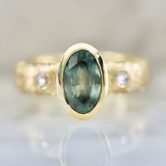 a close up view of a ring with a green stone in the middle and two diamonds on the side