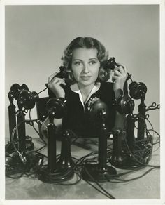 a black and white photo of a woman sitting in front of telephones